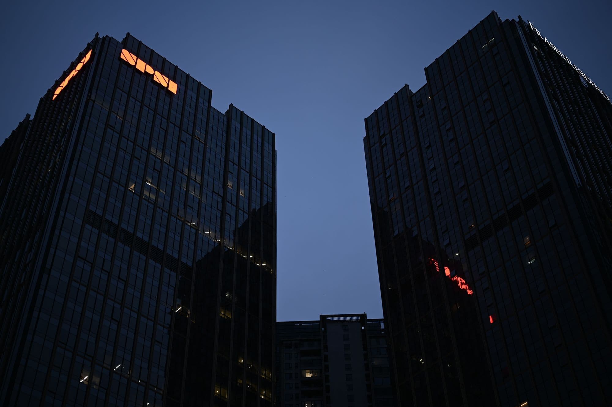 Glass-and-steel towers at blue hour with city lights.